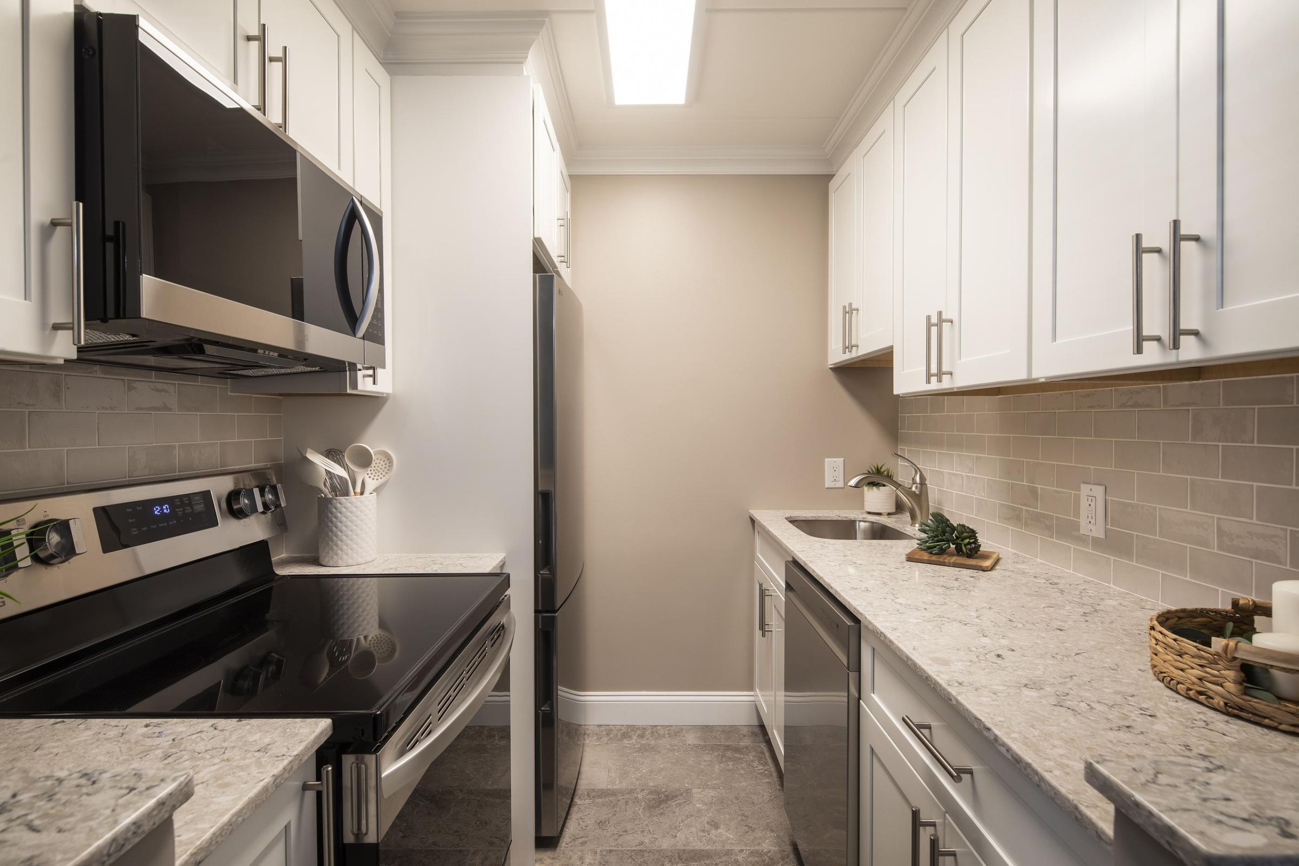 Cadillac Manor Two gray armchairs with pillows sit by a small table in a modern, gray-toned hallway near an elevator.