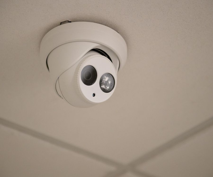 Cadillac Manor A white security camera is mounted on a white ceiling with a grid pattern.