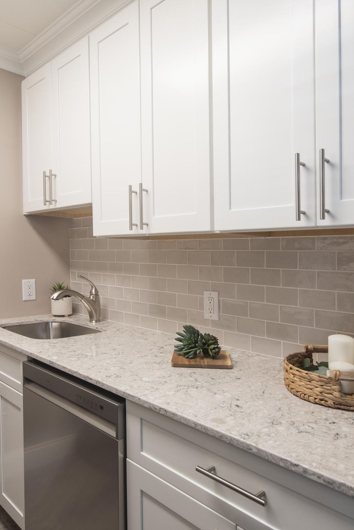 Cadillac Monar Modern kitchen with white cabinets, gray backsplash, and a marble countertop decorated with candles and plants.