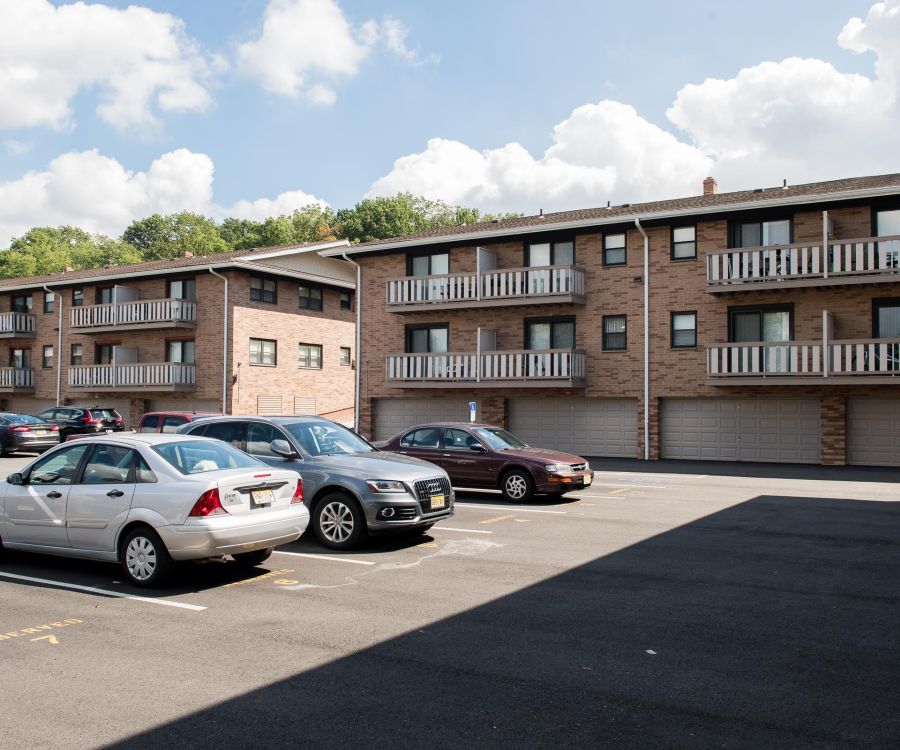 Cambridge Manor Parking lot with several cars in front of two brick apartment buildings on a sunny day.