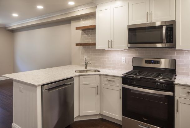 Modern kitchen with white cabinets, stainless steel appliances, and a marble countertop under recessed lighting.