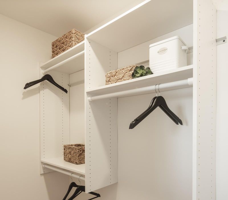 Minimalist walk-in closet with white shelves, black hangers, wicker baskets, and wooden floor.