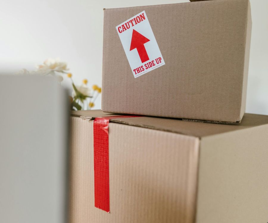 Two cardboard boxes stacked, top box labeled “Caution This Side Up” with an upward red arrow.