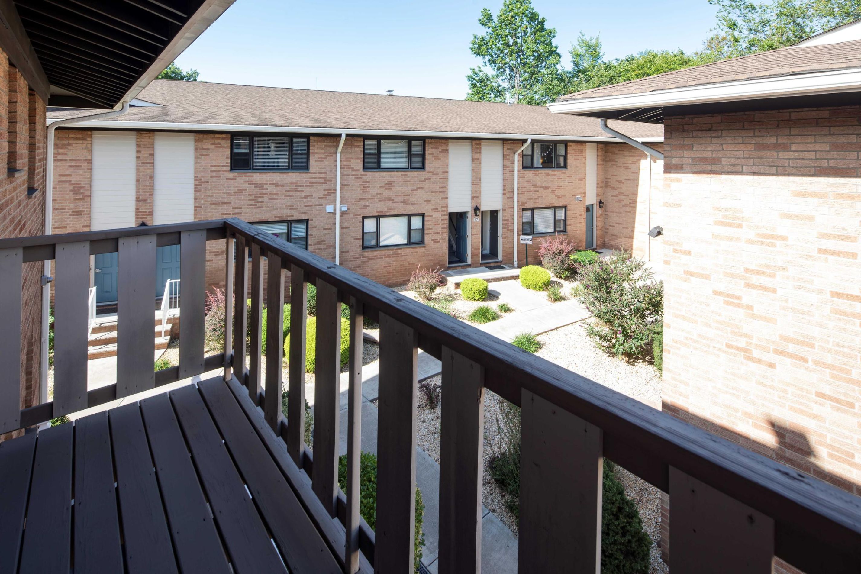Cambridge Manor View from a balcony overlooking a courtyard and brick apartment buildings with some greenery.