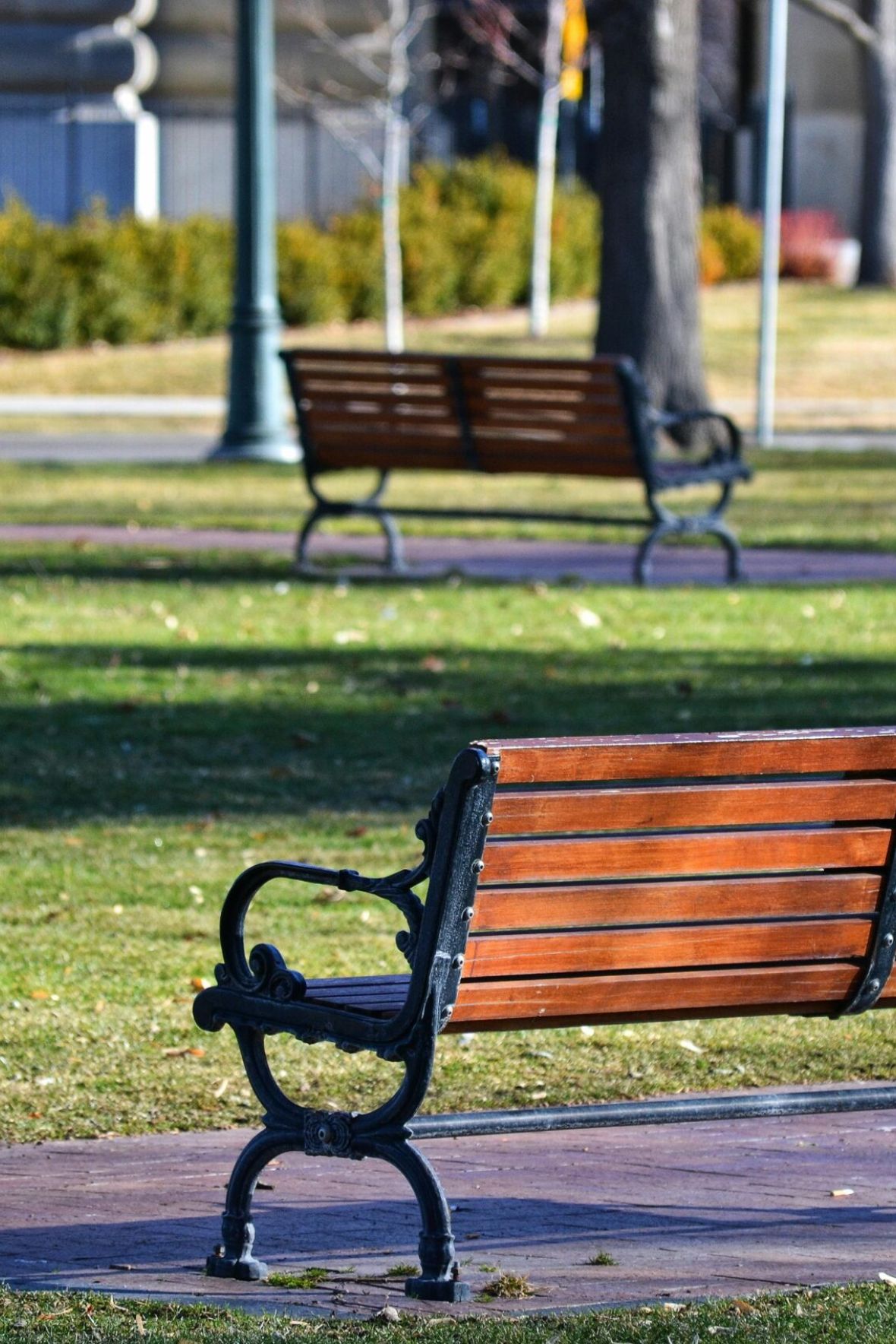 Cambridge Manor Empty outdoor tennis court with nets, surrounded by trees and buildings, under a partly cloudy sky.
