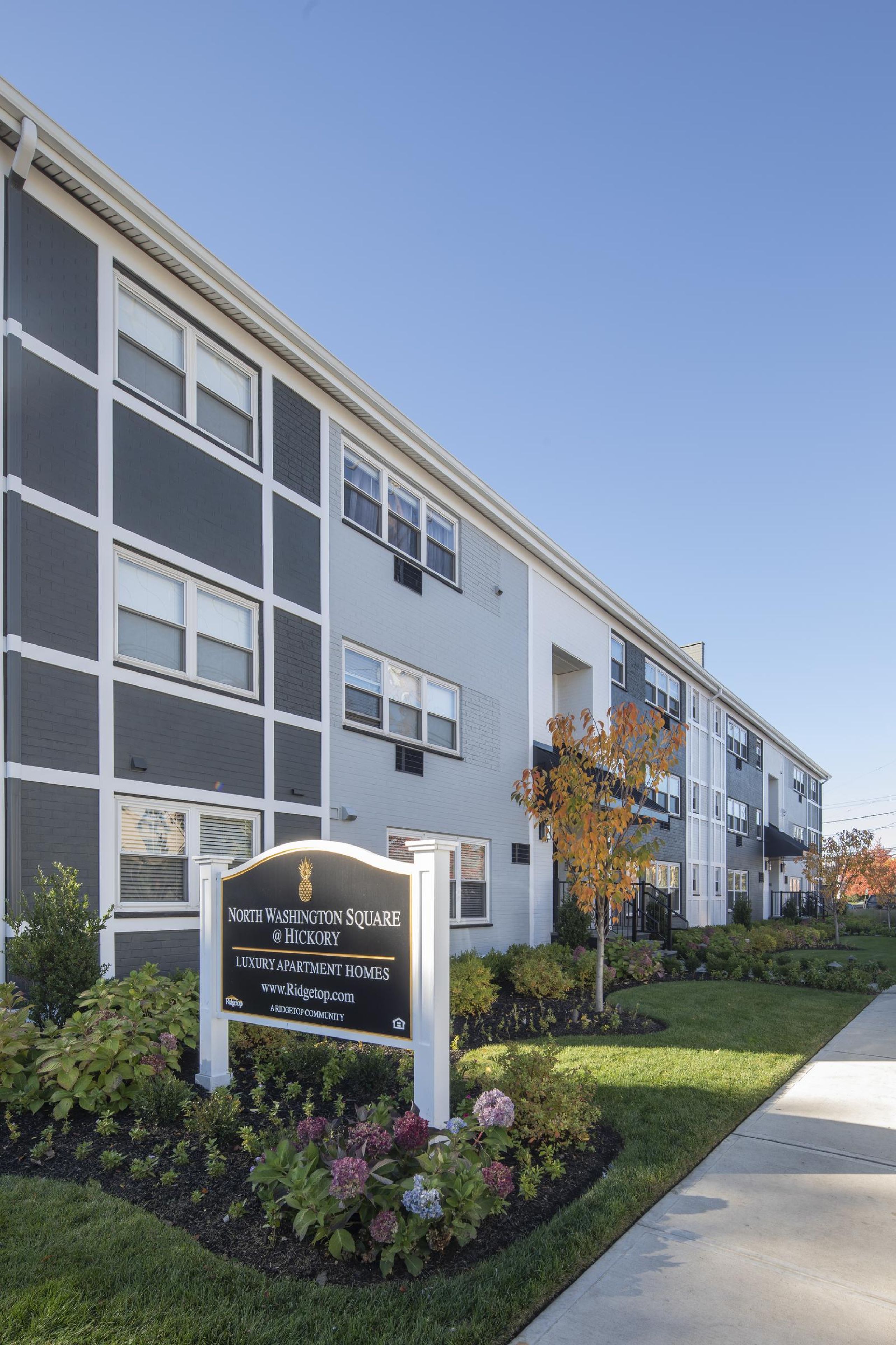 Hickory Manor A modern apartment building with landscaped gardens and a wooden entrance canopy under a partly cloudy sky.