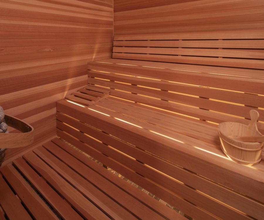 Hickory Manor Interior of a wooden sauna with tiered benches, a bucket with a ladle, and sauna stones in the corner.