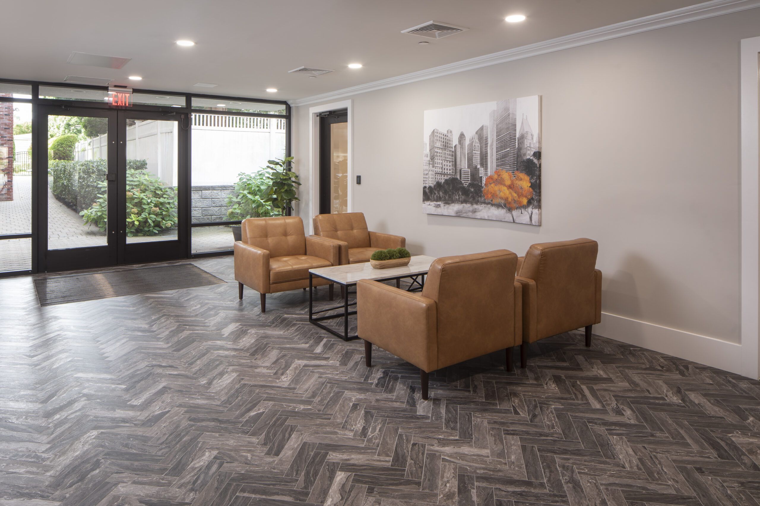 Legion Manor Two gray armchairs with pillows sit by a small table in a modern, gray-toned hallway near an elevator.