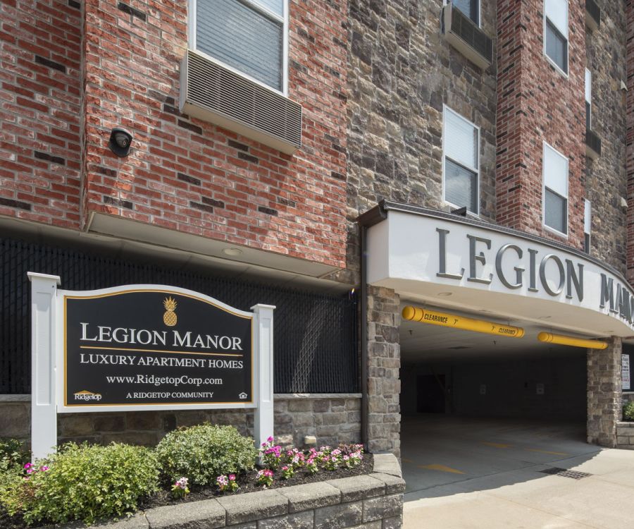 Entrance of Legion Manor luxury apartment building with sign and brick exterior.