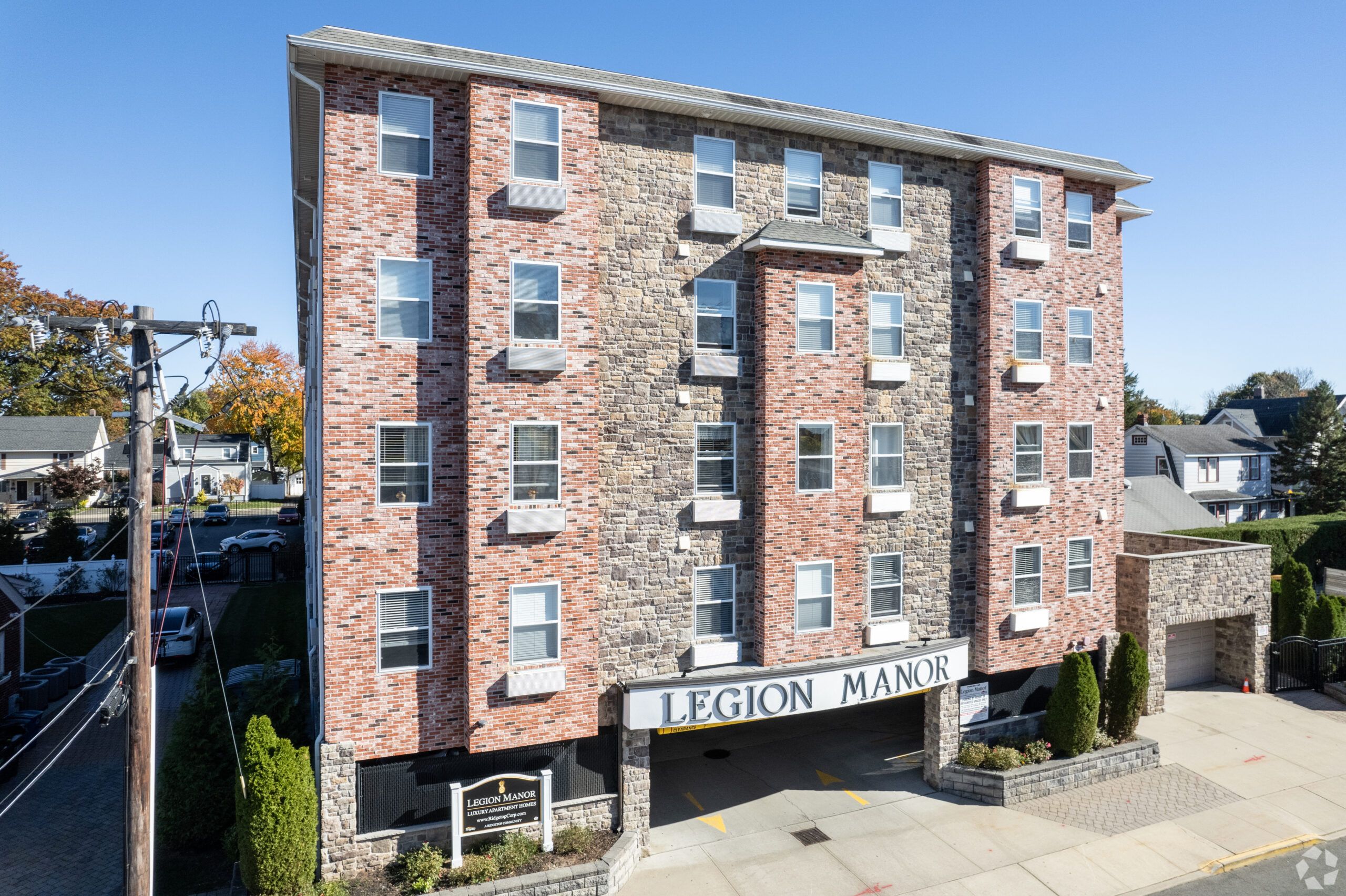 Legion Manor A modern apartment building with landscaped gardens and a wooden entrance canopy under a partly cloudy sky.