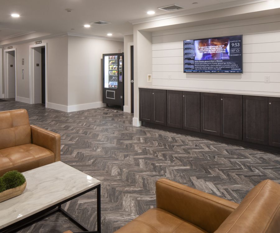 Modern lounge area with tan leather chairs, a TV on the wall, and a vending machine in the background.