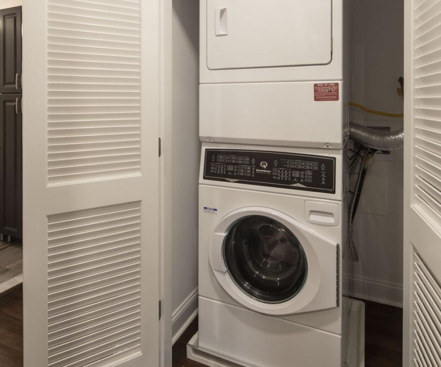 Stacked washer and dryer inside a small closet with louvered doors partially open.