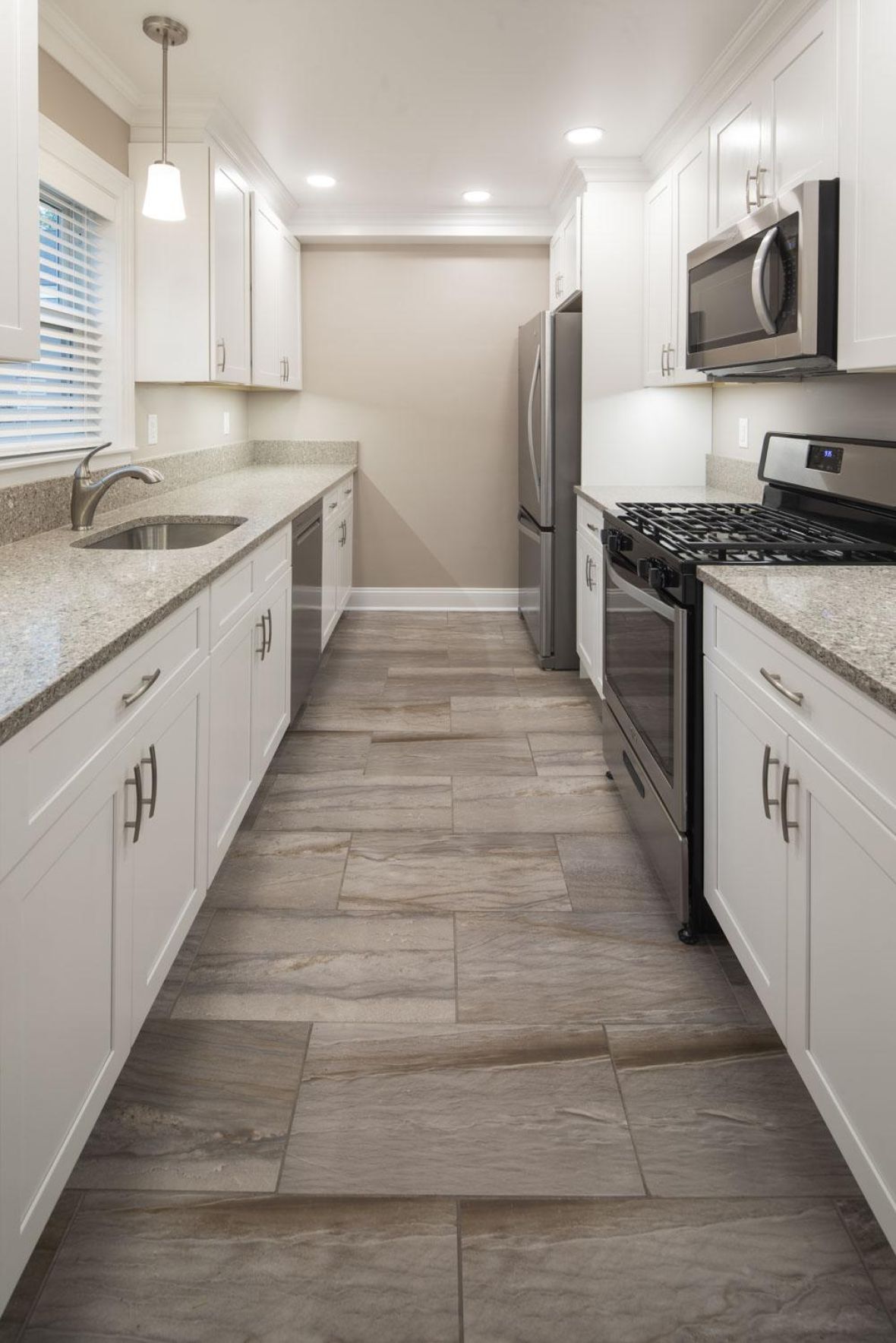 Modern galley kitchen with white cabinets, stainless steel appliances, and light stone tile flooring.