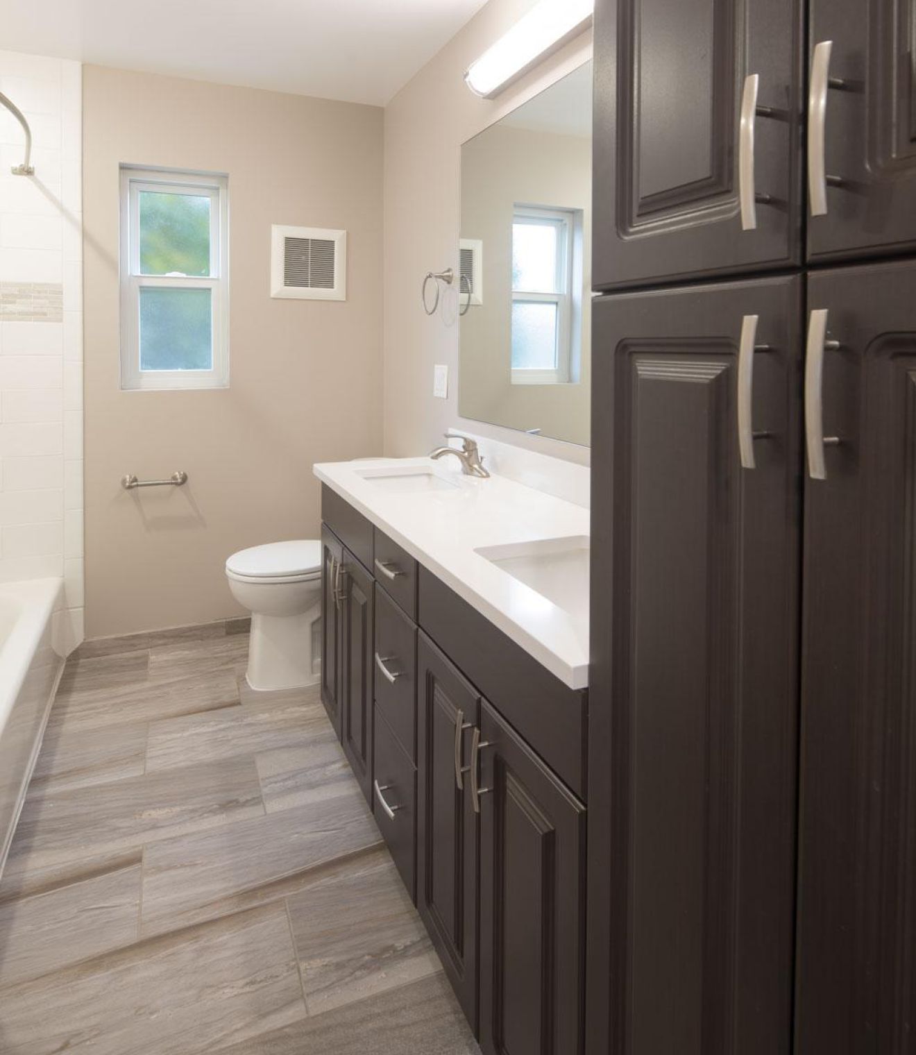 Modern bathroom with dark wood cabinets, double sink, toilet, and grey tile floor.