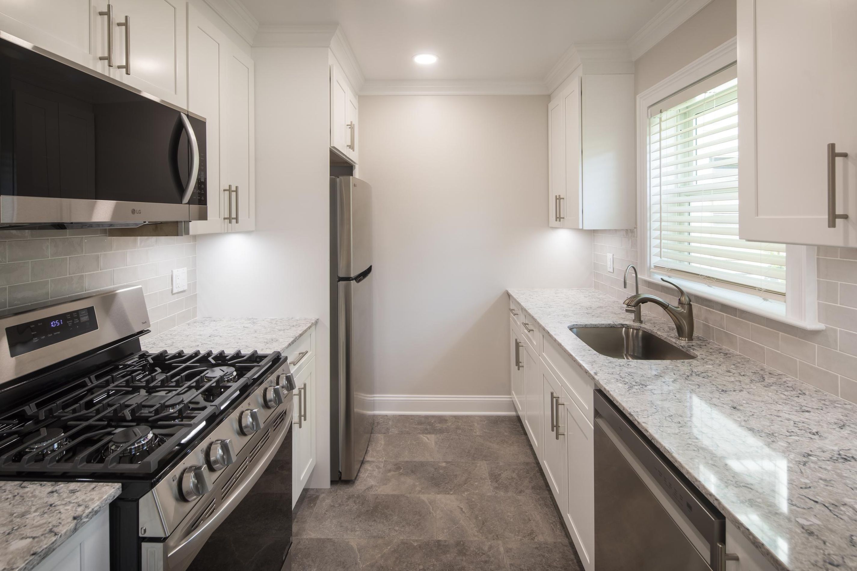 Modern kitchen with stainless steel appliances, white cabinets, granite counters, and a window above the sink.