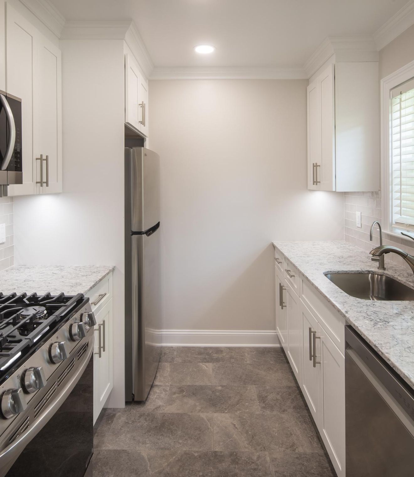Modern kitchen with stainless steel appliances, white cabinets, granite counters, and a window above the sink.
