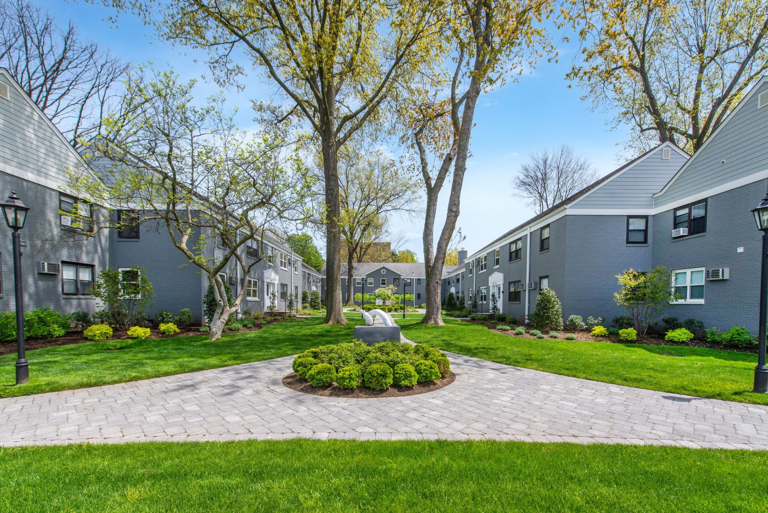 Leonia ManorPatio with wooden pergola, outdoor seating, chairs, and plants, overlooking a green lawn with flags.