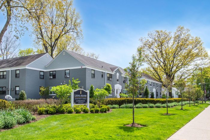 Modern apartment buildings with gray siding, green lawns, trees, and a sign reading "Leonia Manor" in front.