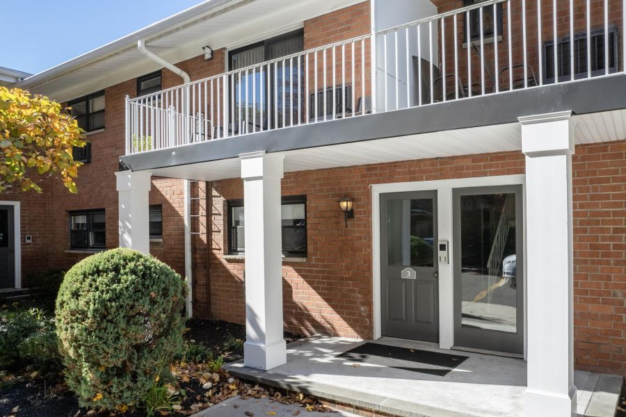 Linden Apartments A digital ButterflyMX intercom system is mounted on a white brick wall next to a wooden corner.