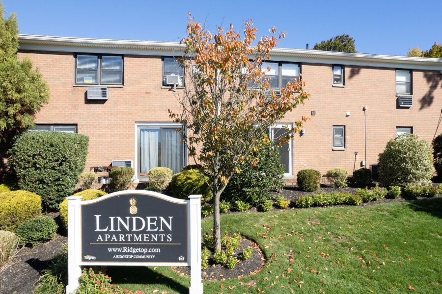 Linden Apartments A modern apartment building with landscaped gardens and a wooden entrance canopy under a partly cloudy sky.
