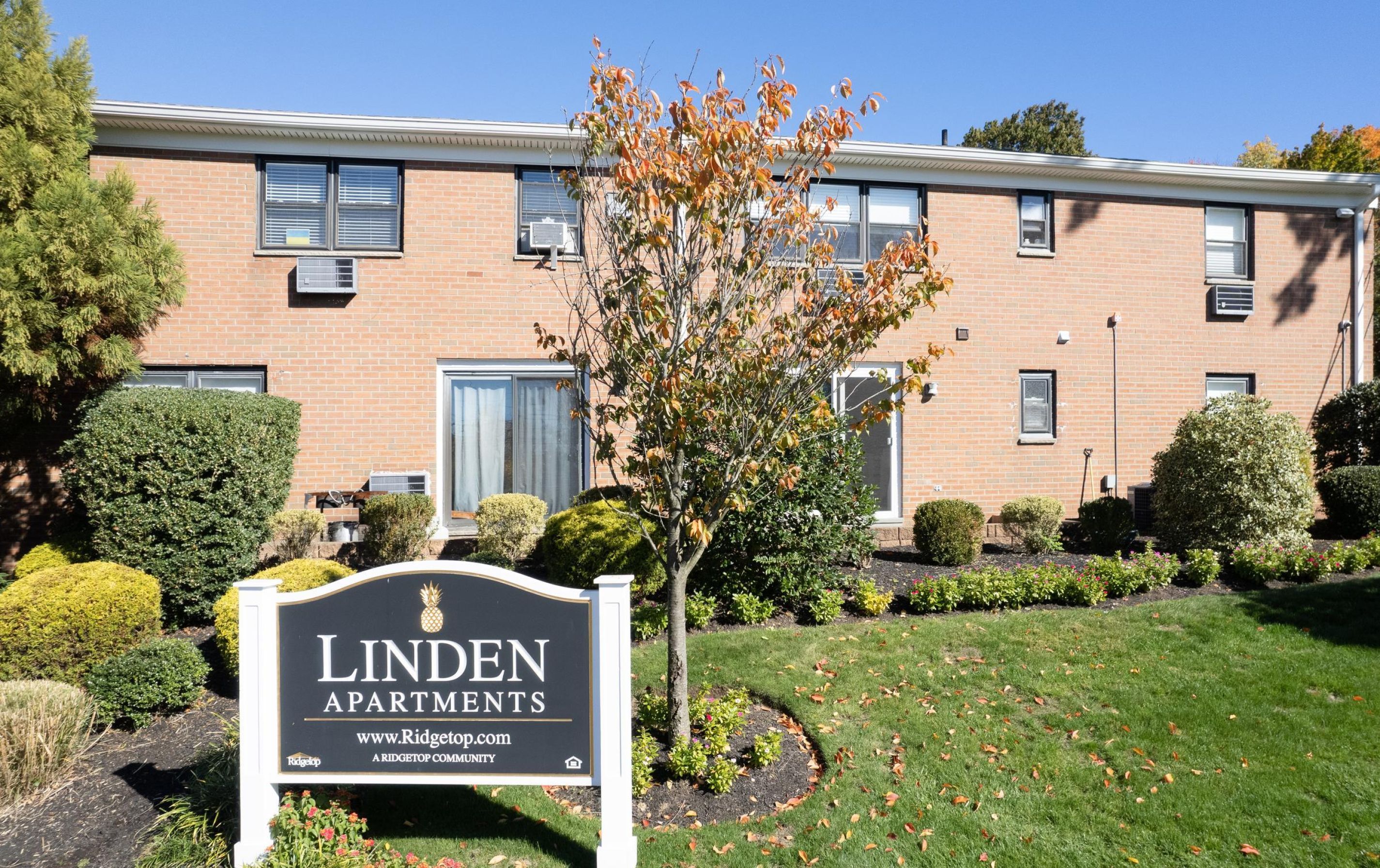 A brick apartment building with manicured bushes and a sign reading "Linden Apartments.