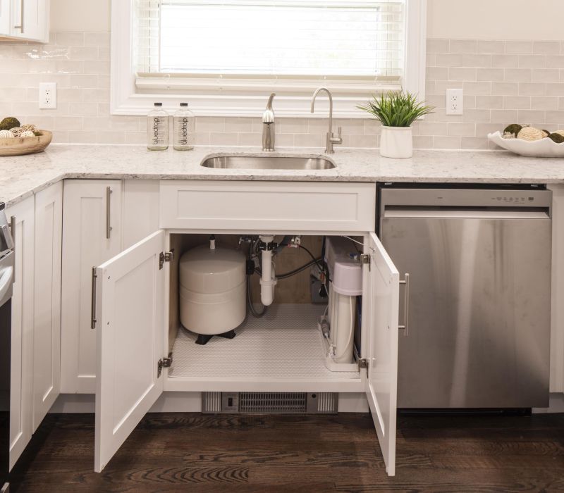 Modern kitchen with cabinet doors open under sink, revealing a water filtration system installed inside.