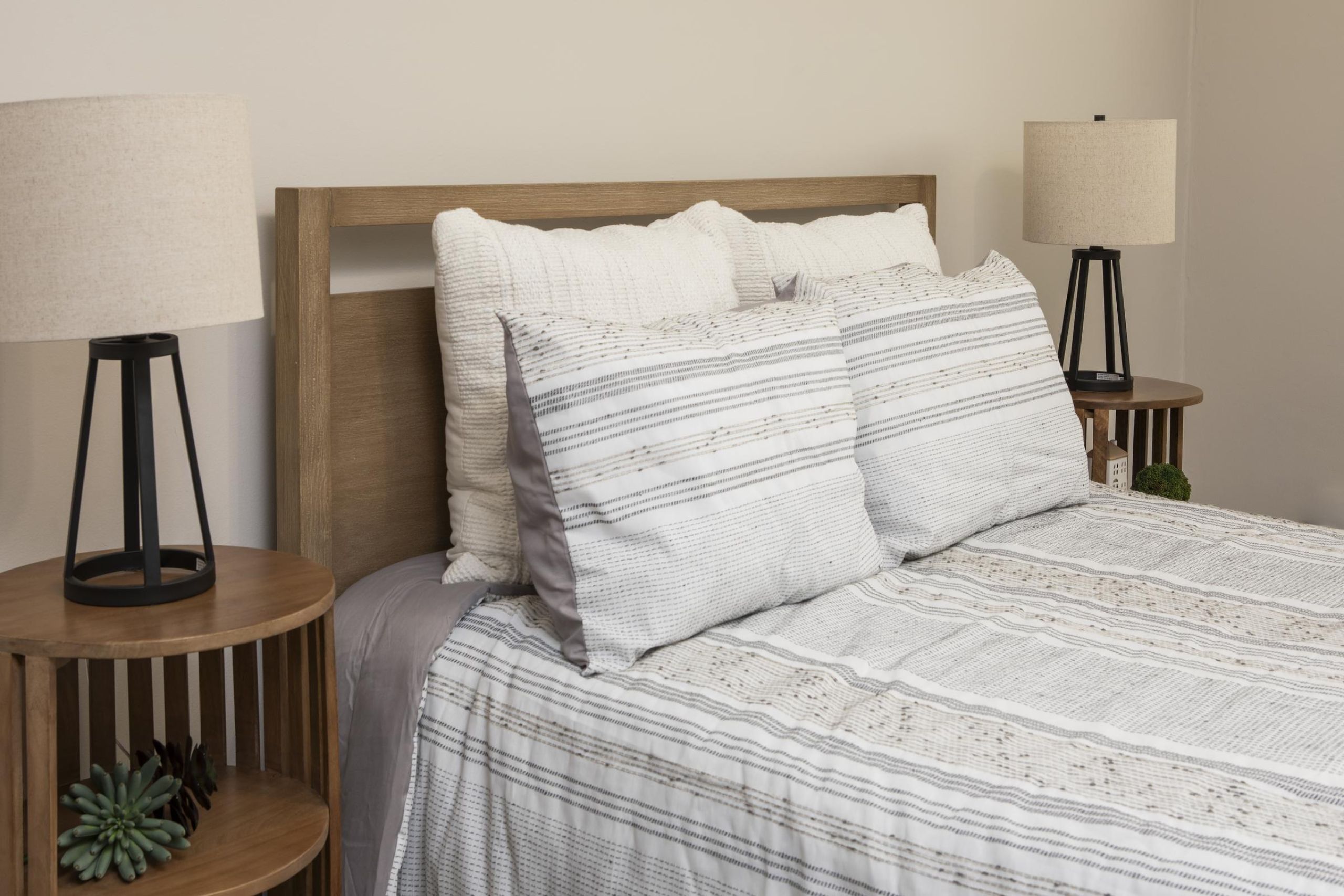 Linden Apartments Two gray armchairs with pillows sit by a small table in a modern, gray-toned hallway near an elevator.