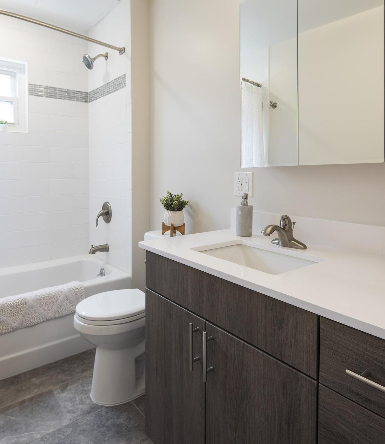 Modern bathroom with white tub, shower curtain, toilet, dark wood vanity, and wall mirror cabinet.