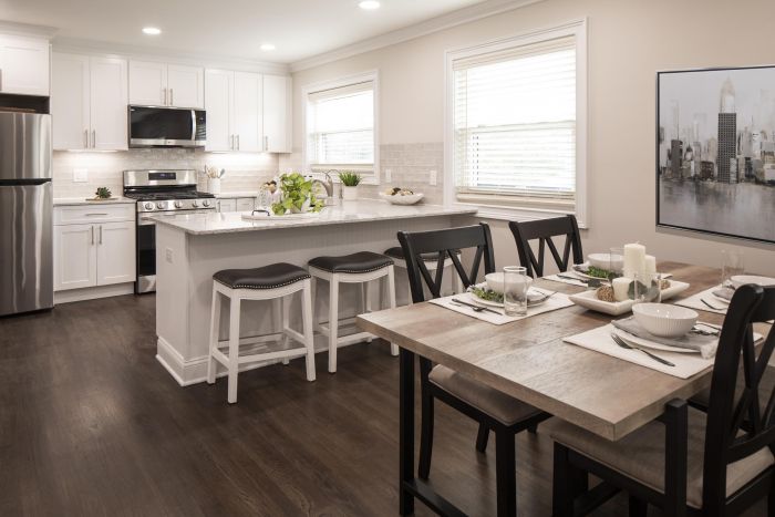 Modern kitchen and dining area with white cabinets, island seating, and a wooden dining table set for four.