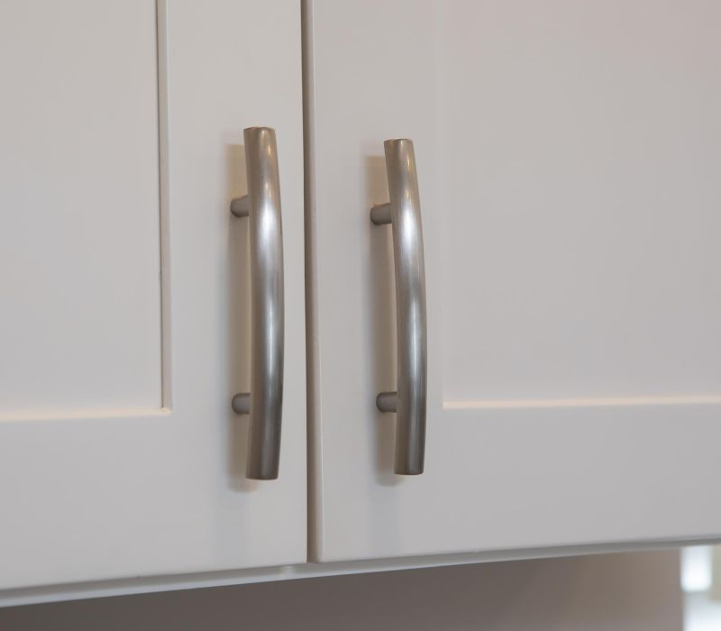 Close-up of two silver handles on white cabinet doors.