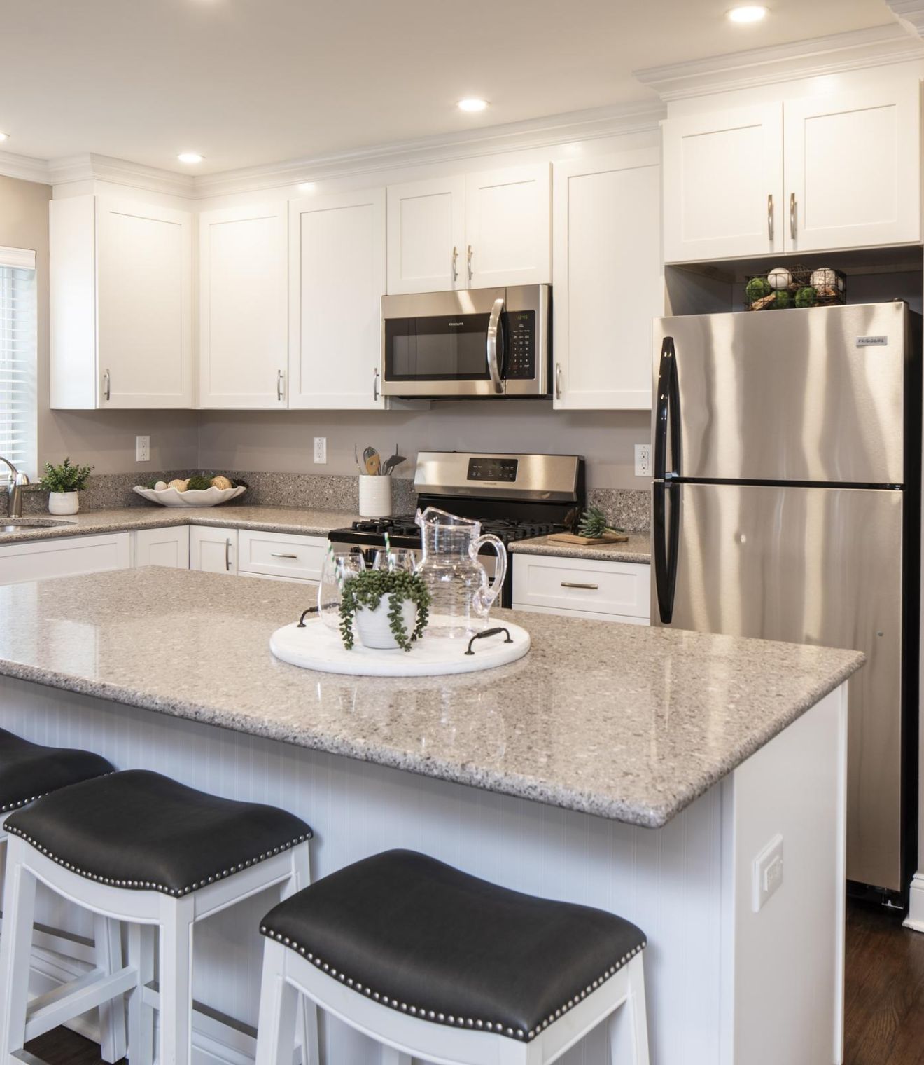 Modern kitchen with white cabinets, stainless steel appliances, and a granite island with three stools.