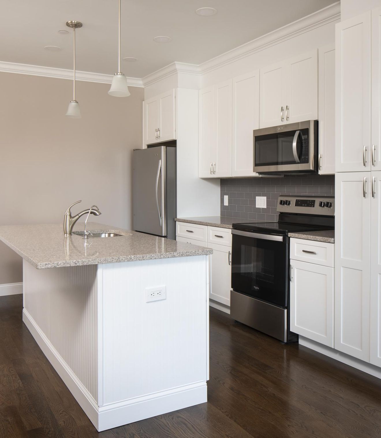 Modern kitchen with white cabinets, stainless steel appliances, and a central island on dark wood flooring.