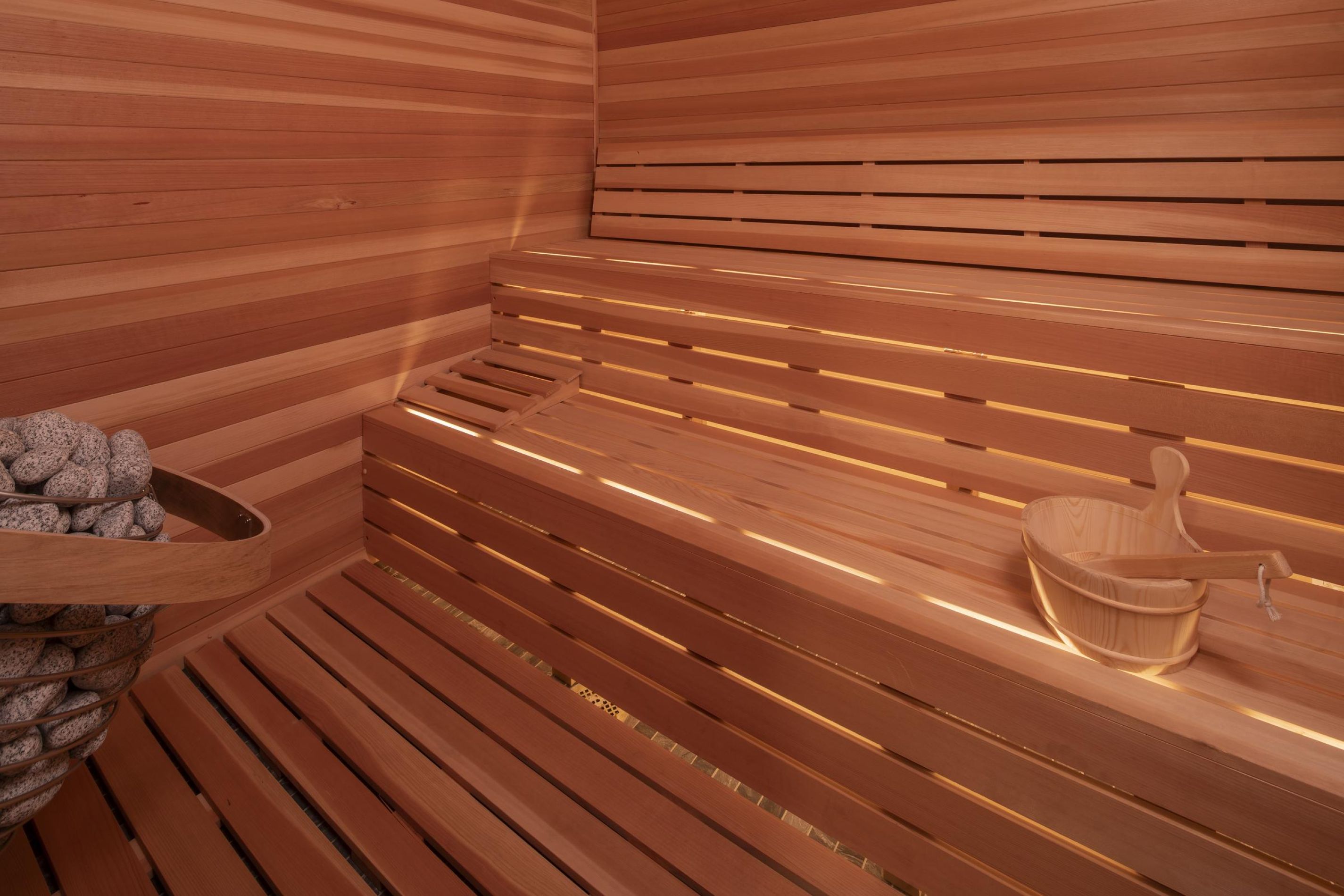 Hickory Manor Interior of a wooden sauna with tiered benches, a bucket with a ladle, and sauna stones in the corner.