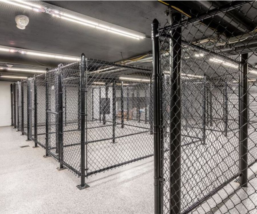 Hickory Manor Indoor storage area with multiple empty chain-link fenced enclosures under fluorescent ceiling lights.
