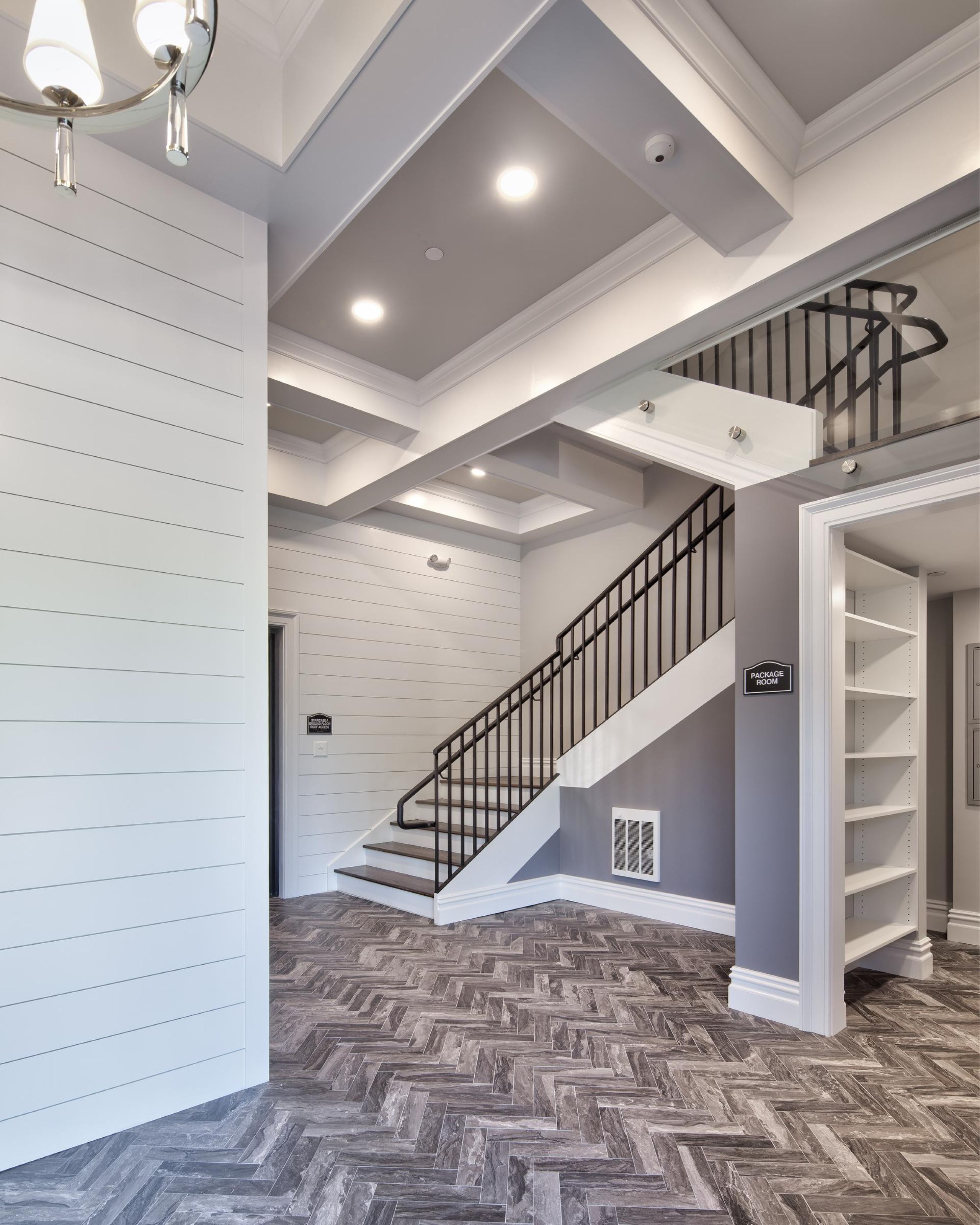 North Washington Square at Hickory Two gray armchairs with pillows sit by a small table in a modern, gray-toned hallway near an elevator.