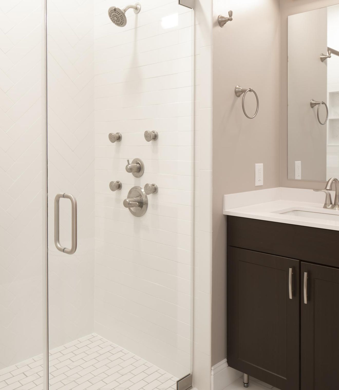 Modern bathroom with a glass shower enclosure and a dark wood vanity with a sink and mirror.