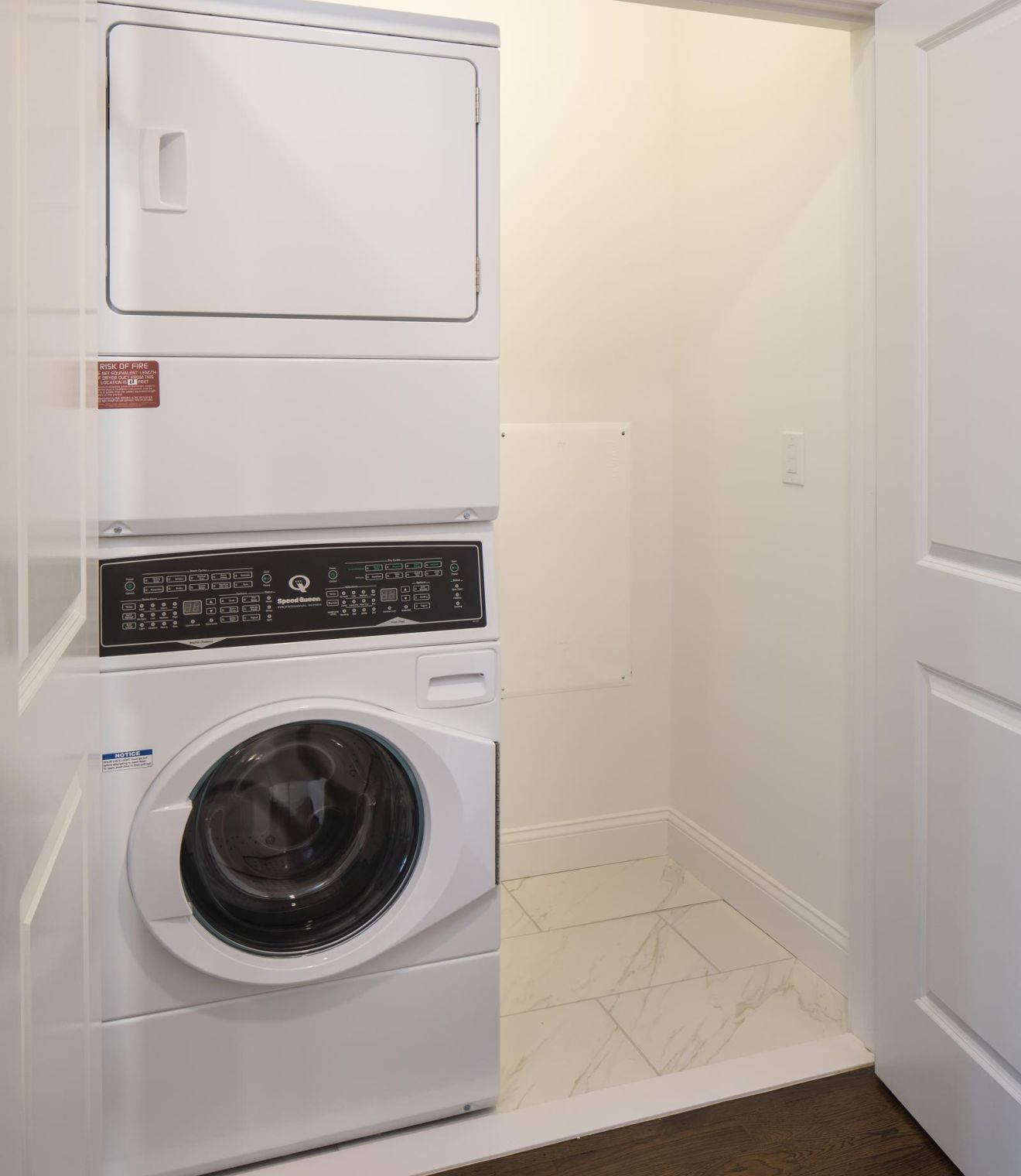 Stacked washer and dryer in a small laundry closet with white walls and tile flooring.