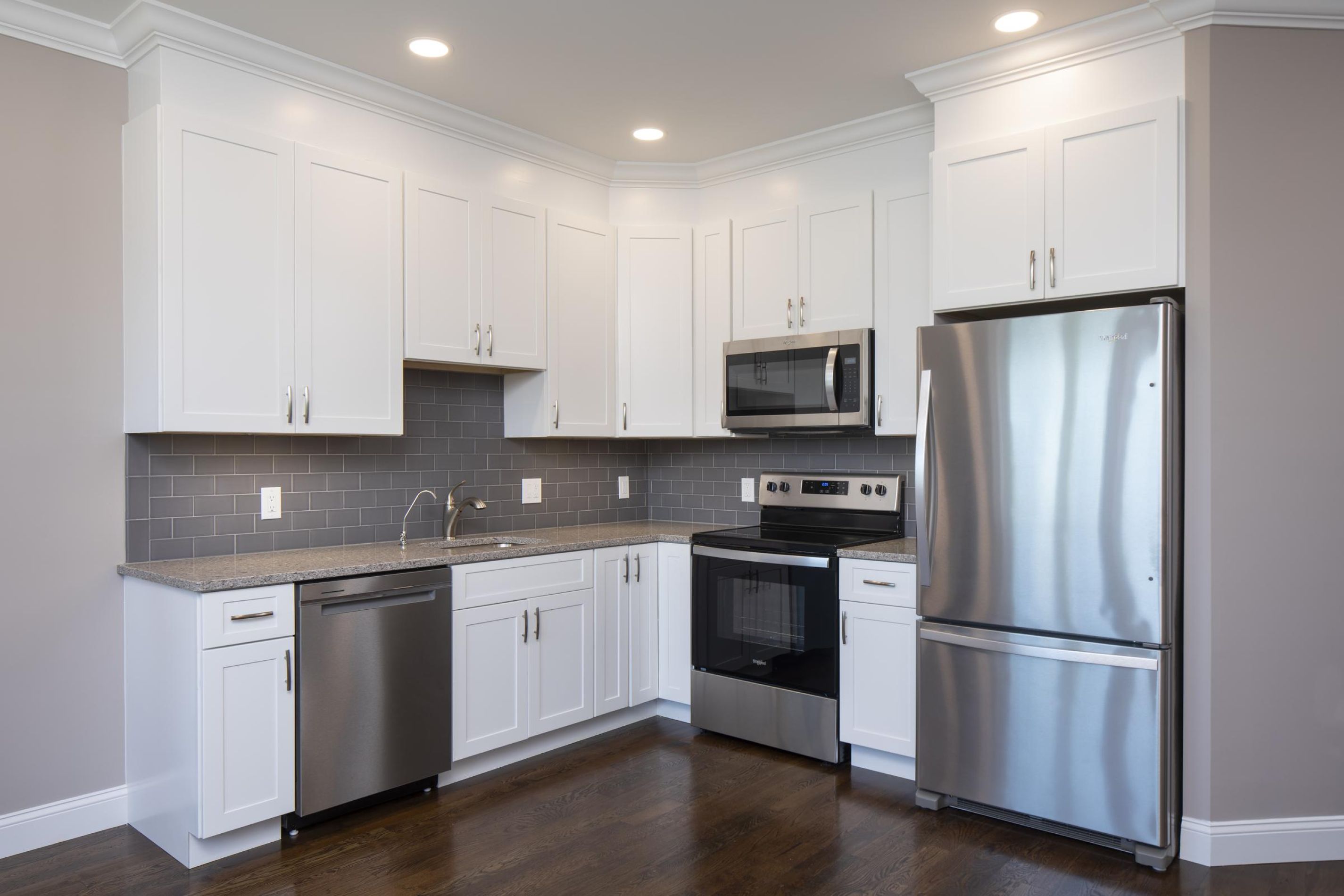 Modern kitchen with white cabinets, stainless steel appliances, gray backsplash, and dark wood floor.