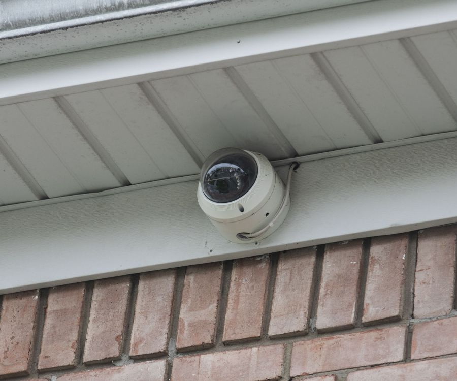 A dome security camera mounted under the eaves of a brick building.