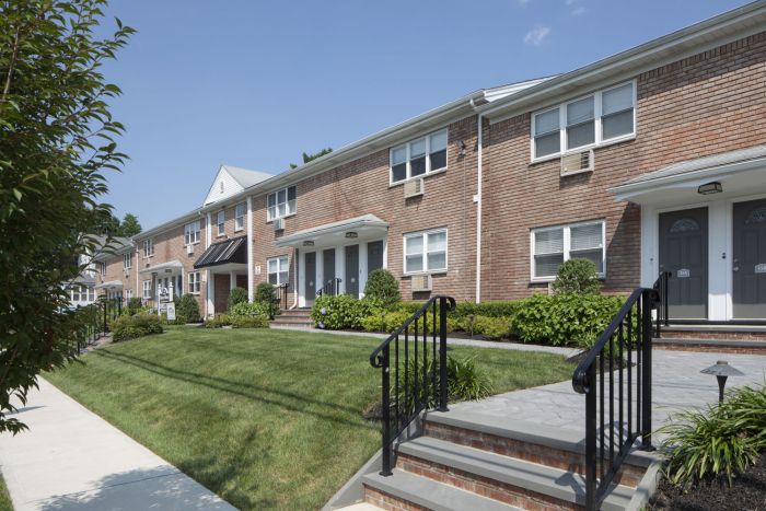 Row of brick townhouses with neatly trimmed lawns and shrubbery on a sunny day.