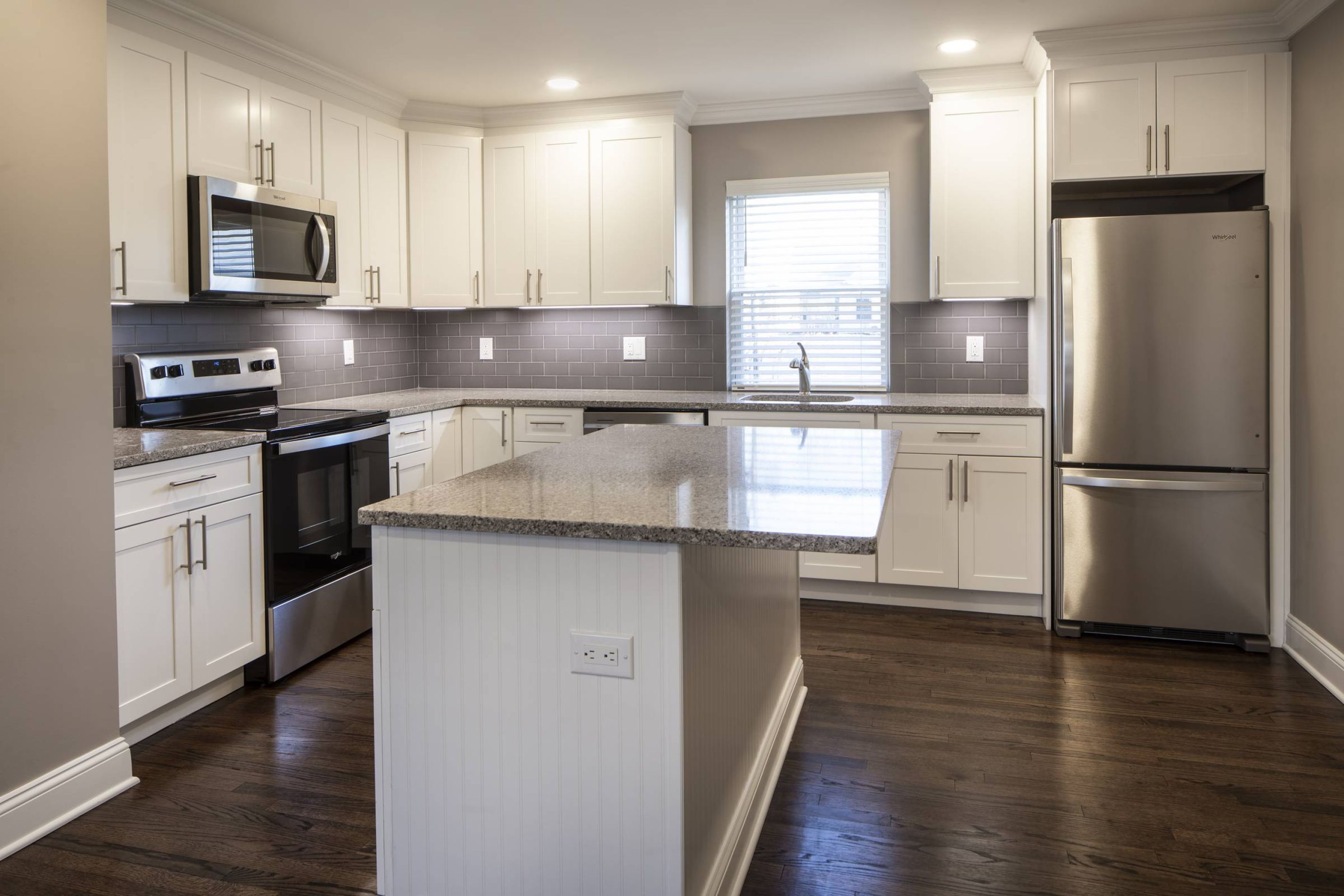 Modern kitchen with white cabinets, stainless steel appliances, granite countertop, and dark wood flooring.