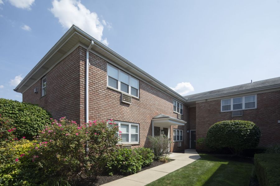 Regency Manor A digital ButterflyMX intercom system is mounted on a white brick wall next to a wooden corner.