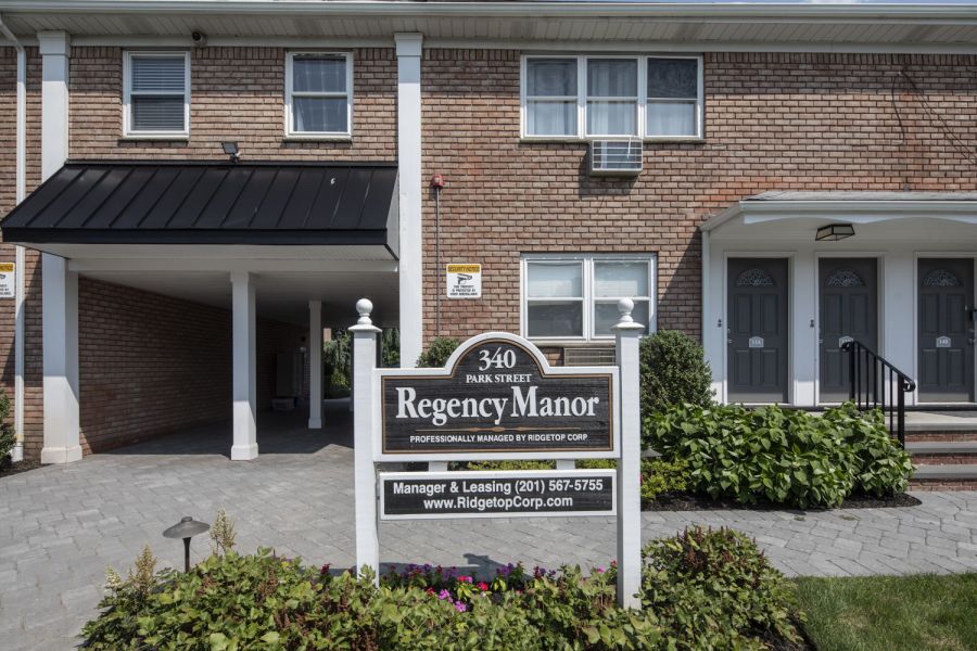 Regency Manor A modern apartment building with landscaped gardens and a wooden entrance canopy under a partly cloudy sky.