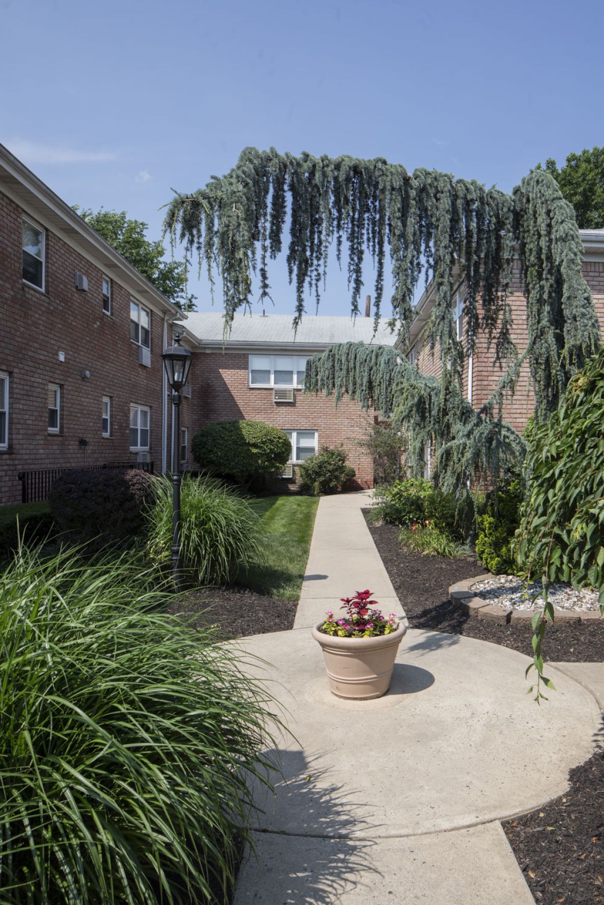 Regency Manor A vintage clock stands in a plaza with blooming trees and a domed building in the background.