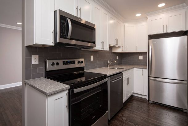 Modern kitchen with stainless steel appliances, white cabinets, gray tile backsplash, and dark wood flooring.