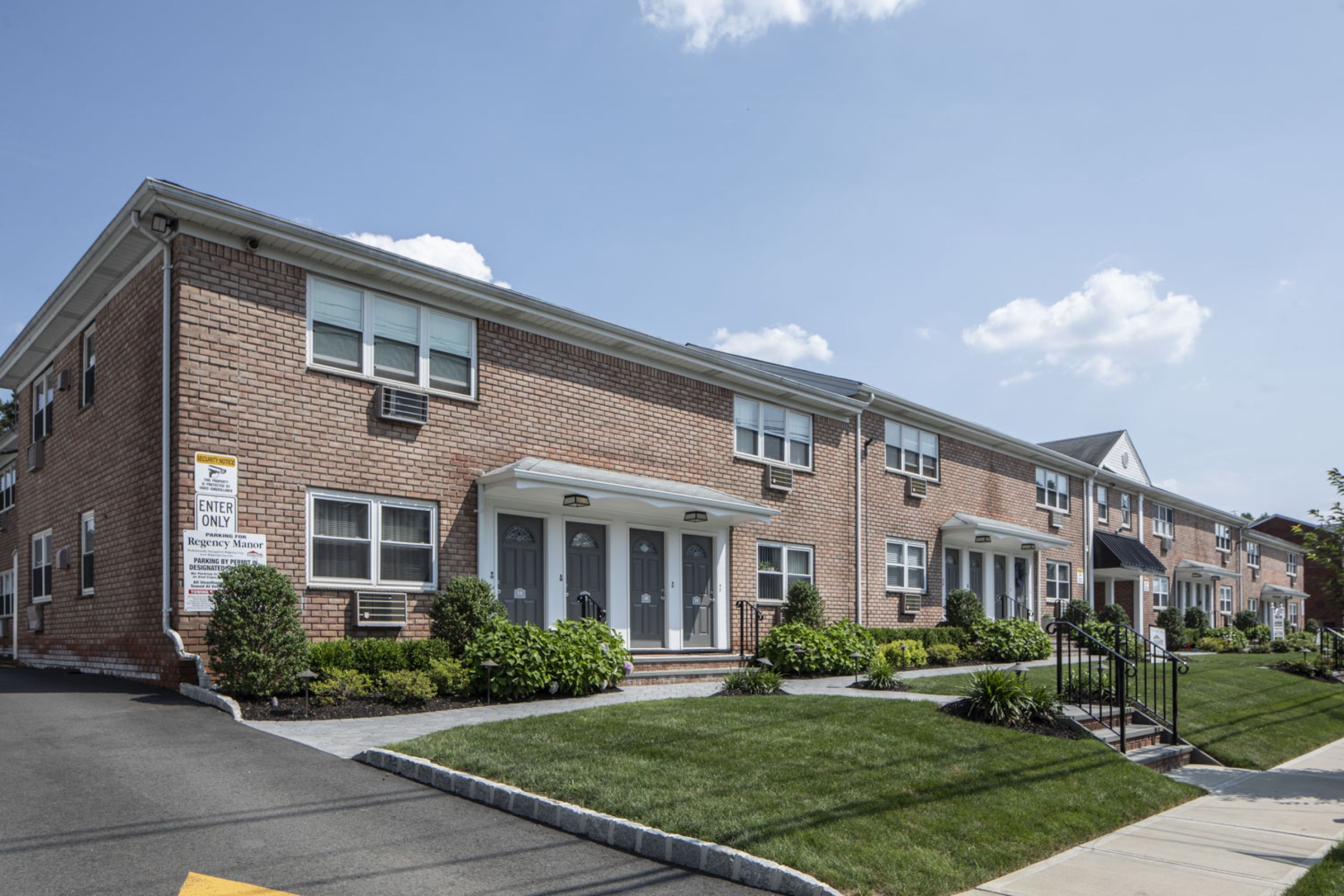 Regency Manor A modern apartment building with landscaped gardens and a wooden entrance canopy under a partly cloudy sky.
