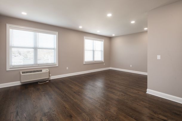 Empty room with wooden floors, beige walls, two large windows, and a wall-mounted air conditioning unit.