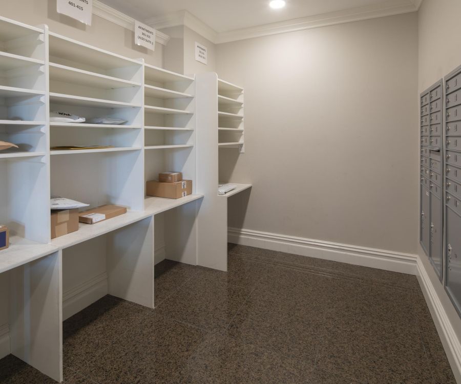 The Atrium Mailroom with sorting shelves holding packages and a wall of gray mailboxes on the right side.
