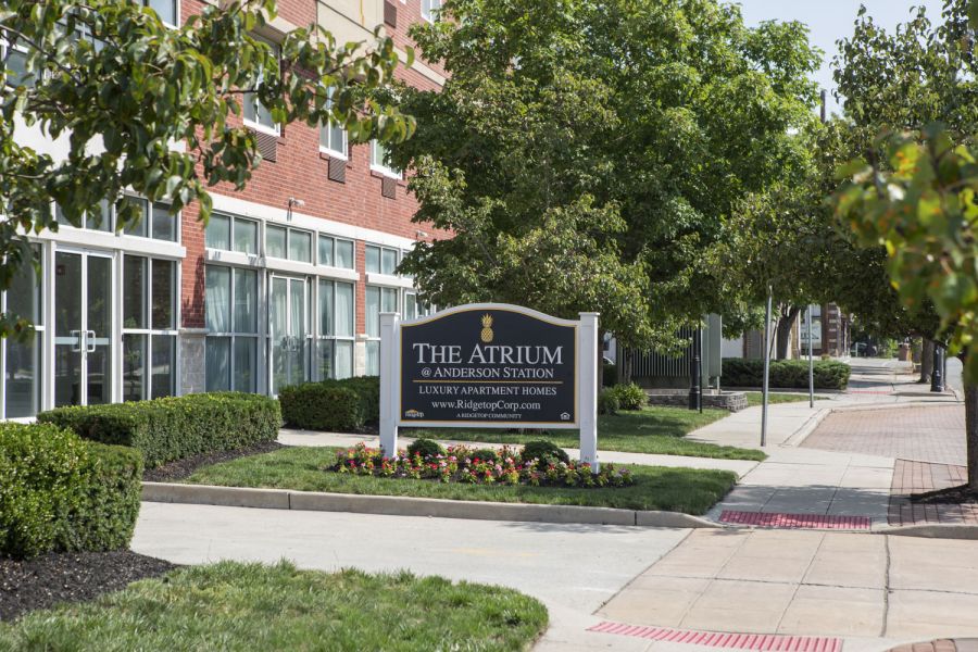 The Atrium A modern apartment building with landscaped gardens and a wooden entrance canopy under a partly cloudy sky.