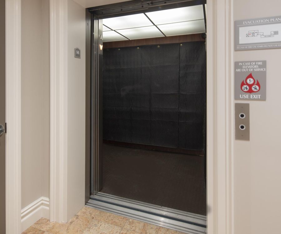 The Atrium Open elevator with black interior, bright ceiling lights, and beige tile floor in a hallway.